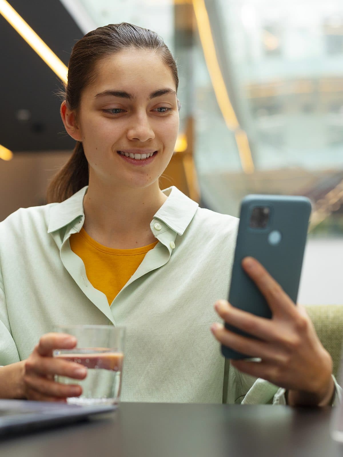 Trabalhadora sorrindo ao usar o celular, sentada à mesa de trabalho com o notebook aberto
