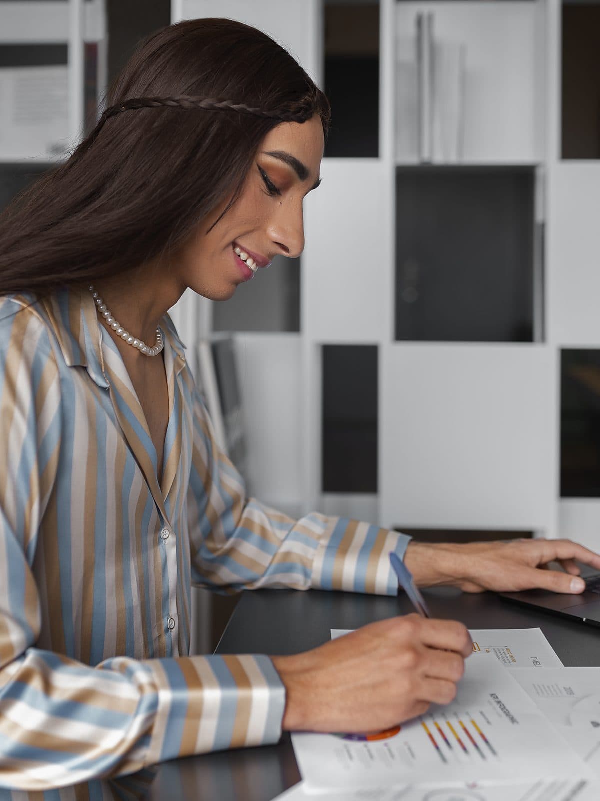 Profissional anotando em relatórios financeiros impressos, ao lado do notebook