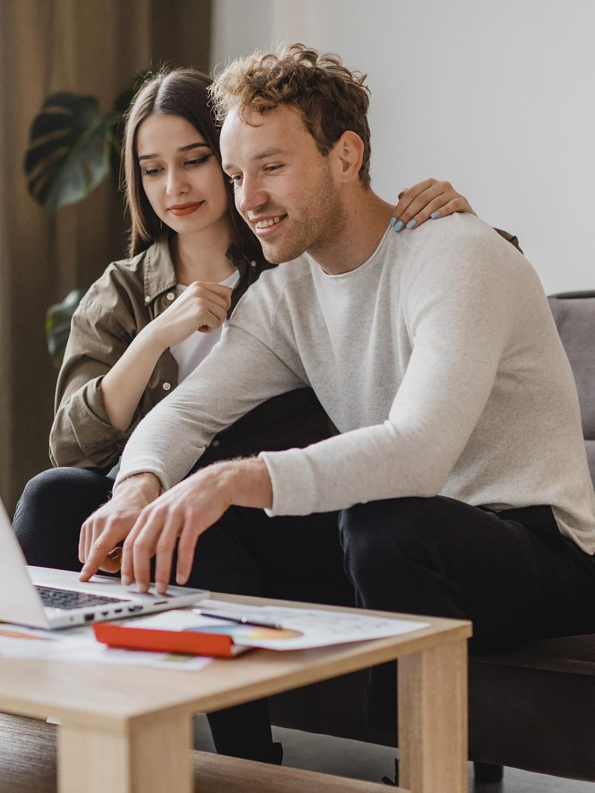 Casal sentado no sofá de casa organizando as contas do mês no notebook